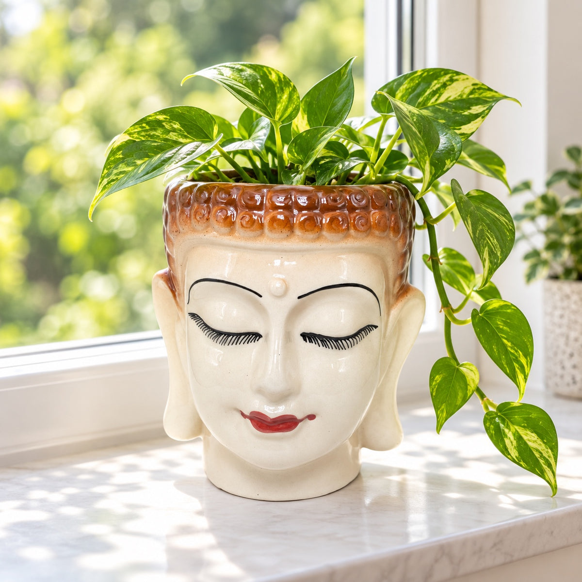 Large Buddha face ceramic indoor planter styled with a pothos plant by a bright window